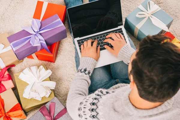 Overhead view of man sitting between gift boxes and using laptop with blank screen — Stock Photo