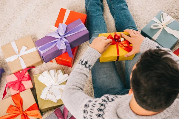 Blick aus der Vogelperspektive auf einen jungen Mann, der auf Teppich sitzt und Weihnachtsgeschenk öffnet — Stockfoto