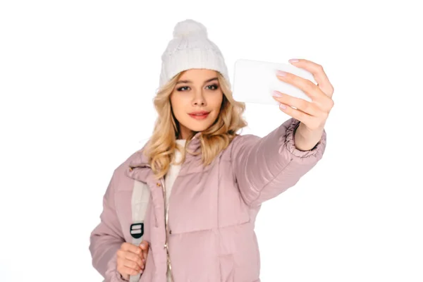 Hermosa joven con mochila tomando selfie con teléfono inteligente aislado en blanco - foto de stock