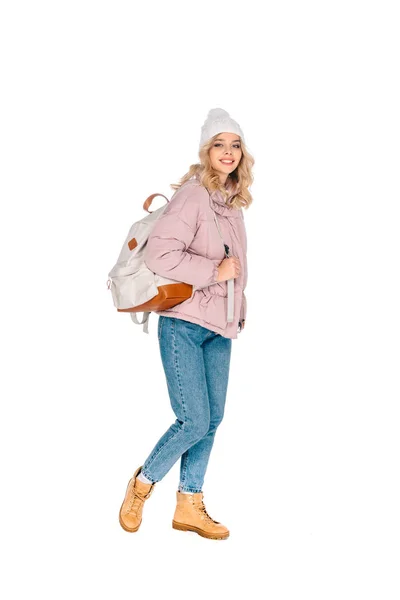 Hermosa joven viajera en sombrero caminando con mochila y sonriendo a la cámara aislada en blanco - foto de stock