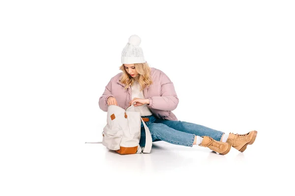 Красива молода жінка в капелюсі сидить і дивиться в рюкзак ізольовано на білому — стокове фото