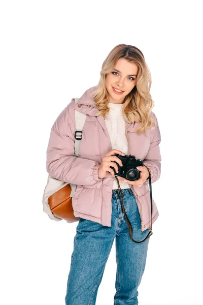 Bela menina sorridente com mochila segurando câmera isolada no branco — Fotografia de Stock