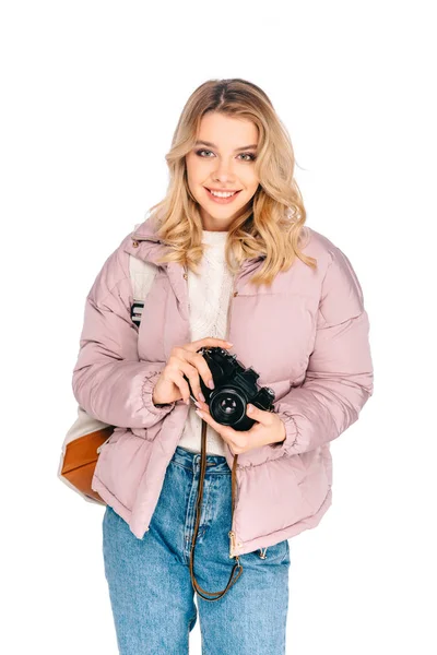 Bela sorridente jovem mulher com mochila segurando câmera isolada no branco — Fotografia de Stock