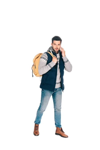 Joven guapo con mochila hablando por teléfono inteligente y mirando la cámara aislada en blanco - foto de stock