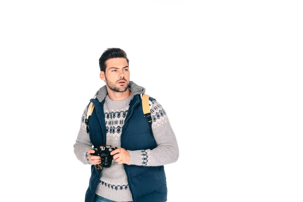 Joven guapo con mochila sosteniendo la cámara y mirando hacia otro lado aislado en blanco - foto de stock