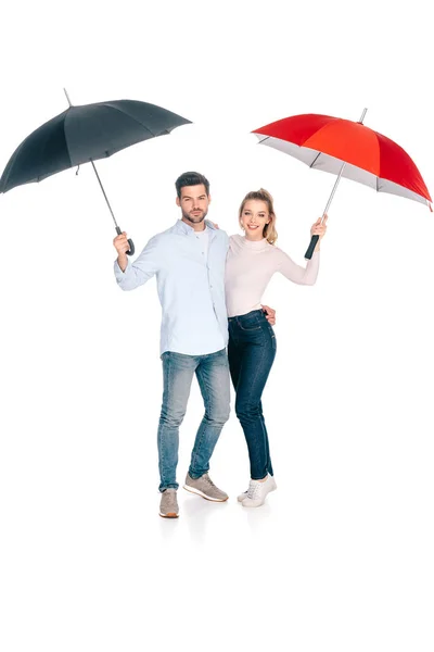 Красивая счастливая молодая пара, держащая зонтики и улыбающаяся в камеру, изолированную на белом — стоковое фото