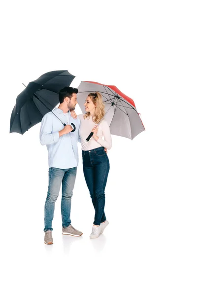 Красива молода пара тримає парасольки і посміхається один одному ізольовано на білому — стокове фото