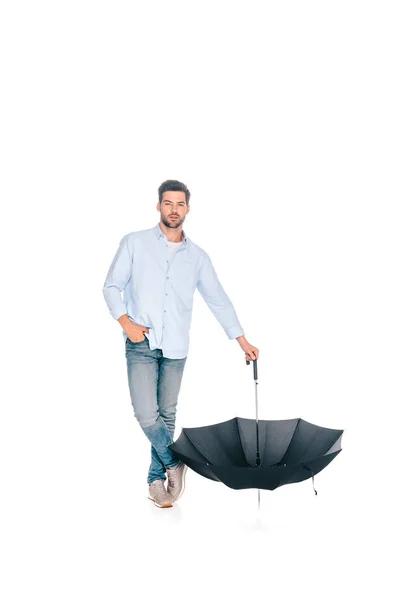 Vista completa de hombre guapo sosteniendo paraguas negro y mirando a la cámara aislada en blanco - foto de stock