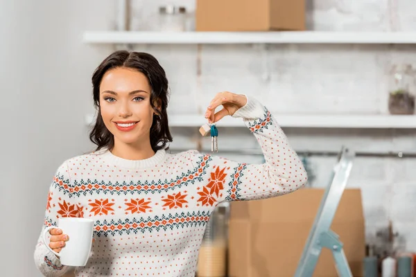 Glückliche junge Frau mit Kaffeetasse zeigt Schlüssel in Küche im neuen Zuhause — Stockfoto