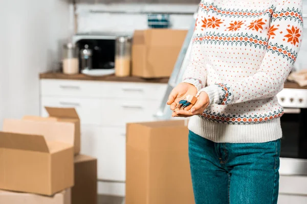 Cropped image of woman holding keys in kitchen with cardboard boxes at new home — Stock Photo