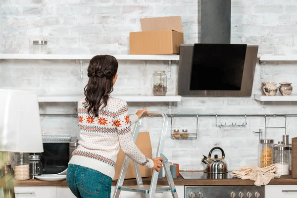 Rear view of woman standing on ladder in kitchen during relocation at new home — Stock Photo