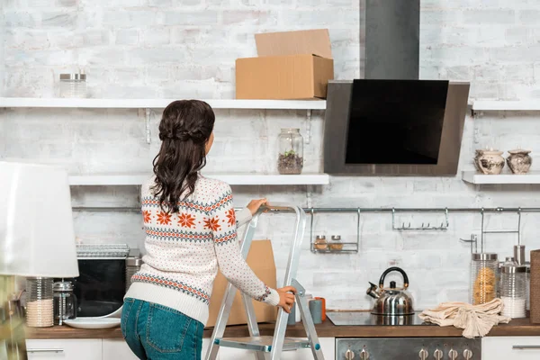 Vista posteriore della donna in piedi sulla scala in cucina durante il trasferimento in una nuova casa — Foto stock