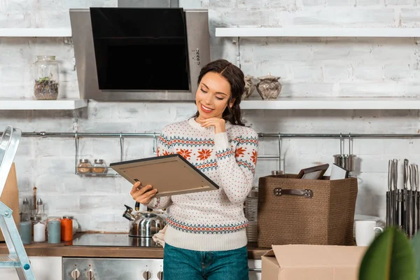 Young smiling woman looking at painting in kitchen during relocation at new home — Stock Photo