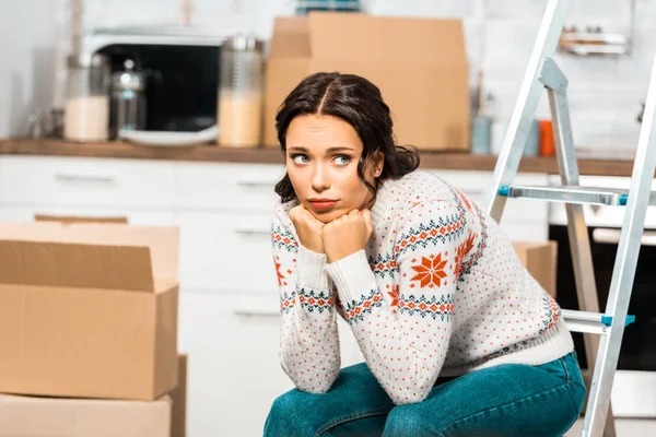 Грустная красивая женщина сидит на лестнице на кухне с картонными коробками во время переезда в новый дом — стоковое фото