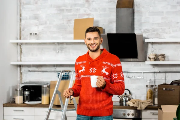 Fröhlicher Mann mit Kaffeetasse zeigt Schlüssel in Küche mit Pappkartons beim Umzug ins neue Zuhause — Stockfoto