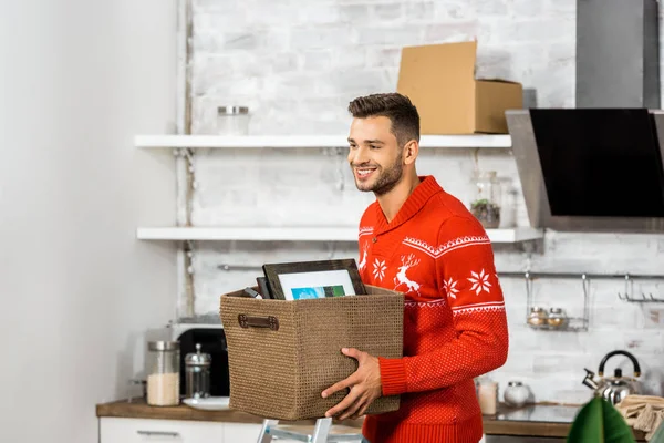 Happy young man carrying box in kitchen during relocation in new home — Stock Photo