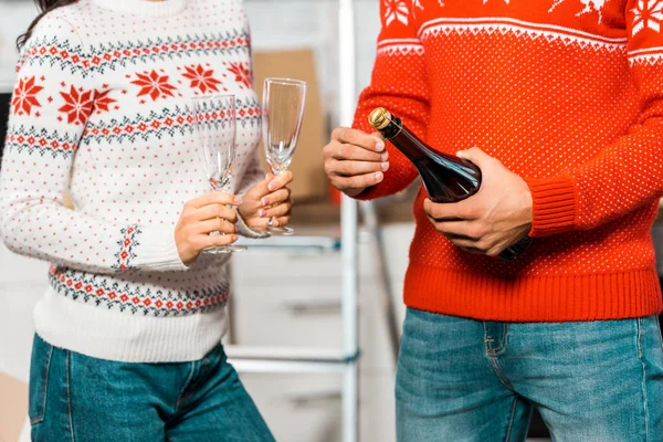 Cropped image of man opening champagne bottle while his girlfriend standing near with glasses for celebration of relocation in new home — Stock Photo