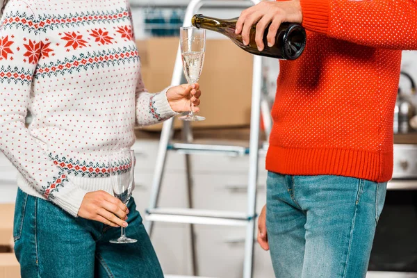Cropped image of man pouring champagne into glass in girlfriend hand in kitchen at new home — Stock Photo