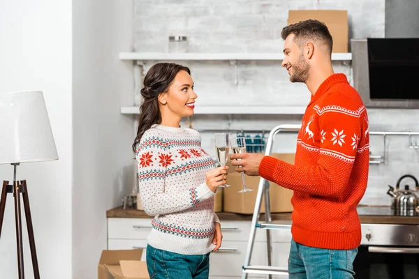 Sonriendo joven pareja tintineo por copas de champán y celebrando la reubicación en nuevo hogar - foto de stock