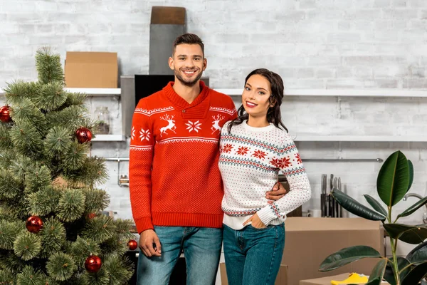 Foyer sélectif de sourire jeune couple debout près de l'arbre de Noël décoré dans la cuisine à la maison — Photo de stock