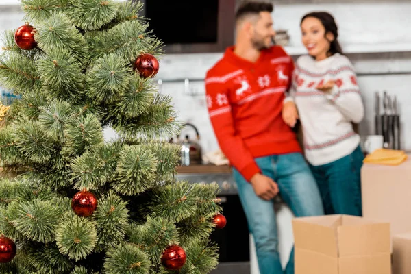 Enfoque selectivo del árbol de Navidad con adornos y pareja de pie detrás de casa - foto de stock
