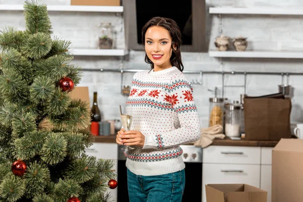 Attrayant femme debout avec verre de champagne près de l'arbre de Noël dans la cuisine à la maison — Photo de stock