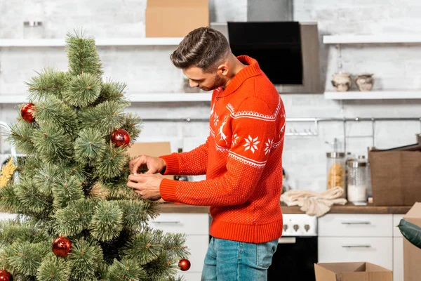 Enfoque selectivo del hombre decorando el árbol de Navidad por bolas en la cocina en casa - foto de stock
