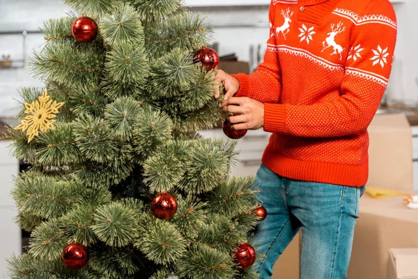 Abgeschnittenes Bild eines Mannes, der den Weihnachtsbaum mit Kugeln in der heimischen Küche schmückt — Stockfoto