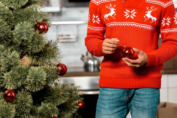 Imagen recortada de hombre decorando árbol de Navidad por bolas en casa - foto de stock