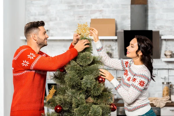 Seitenansicht eines glücklichen jungen Paares, das zu Hause den Weihnachtsbaum schmückt — Stockfoto