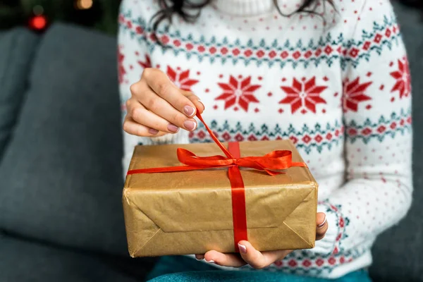 Vista parziale della donna che slega la scatola regalo di Natale sul divano a casa — Foto stock