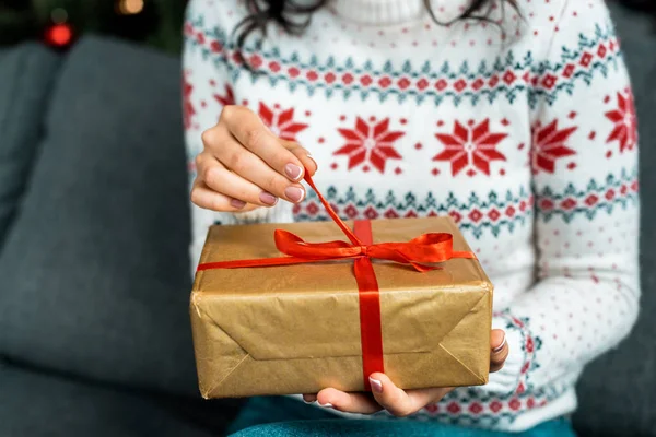 Teilansicht einer Frau, die zu Hause auf dem Sofa Weihnachtsgeschenkschachtel löst — Stockfoto