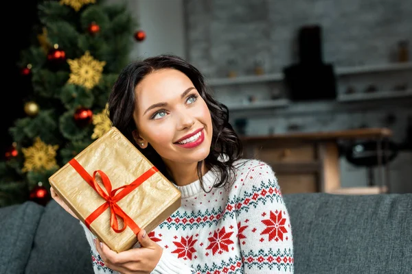 Foyer sélectif de la jeune femme à l'écoute de boîte cadeau sur le canapé près de l'arbre de Noël à la maison — Photo de stock