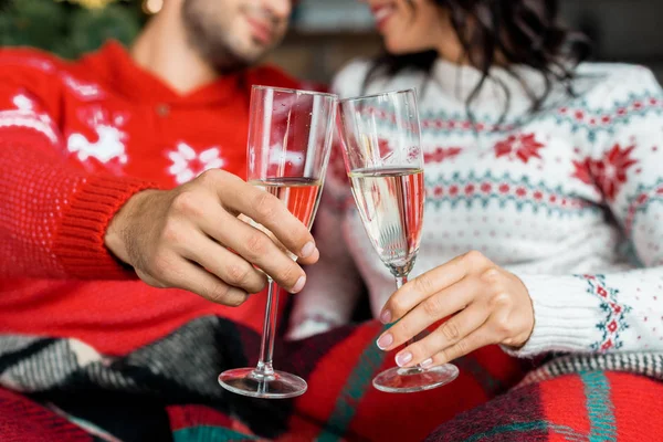 Vista parcial de la pareja celebrando la Navidad y tintineo por copas de champán en el sofá en casa - foto de stock
