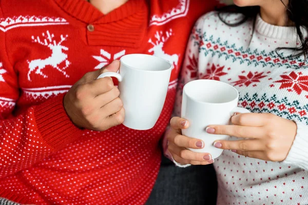 Обрезанное изображение пары, держащей чашки горячего кофе на диване дома — стоковое фото