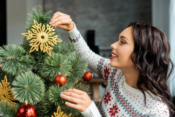 Vista lateral de mujer atractiva decorando árbol de Navidad en casa - foto de stock