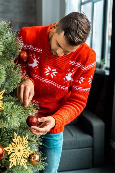 Young man decorating christmas tree by baubles at home — Stock Photo