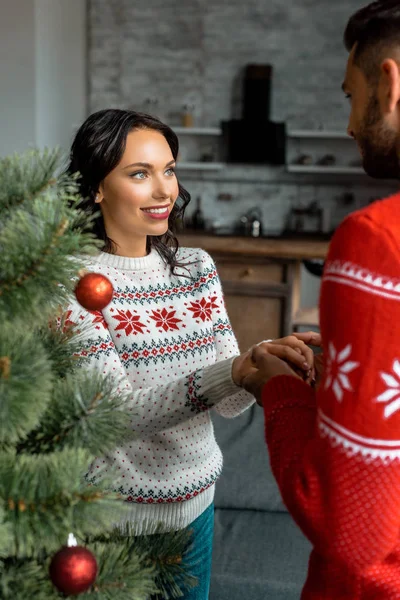 Mann hält Hand seiner Freundin in der Nähe des geschmückten Weihnachtsbaums — Stockfoto