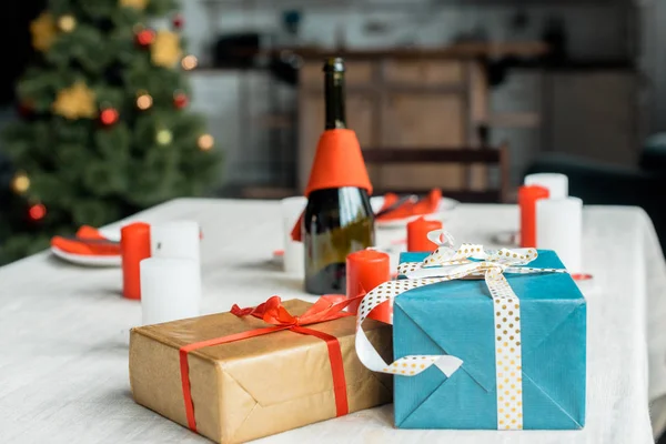 Foco seletivo de caixas de presente de Natal na mesa servida com velas e garrafa de champanhe — Fotografia de Stock
