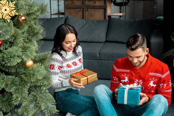 Young couple sitting with gift boxes near christmas tree at home — Stock Photo