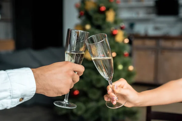 Imagen recortada de pareja celebrando la Navidad y tintineo por la copa de champán en casa - foto de stock