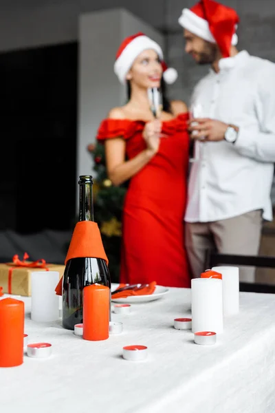Foyer sélectif de bouteille de champagne avec des bougies à la table de Noël servi et couple célébrant avec des verres de champagne derrière à la maison — Photo de stock