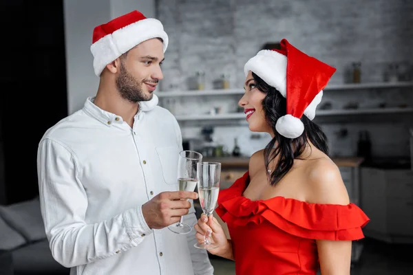 Jovem casal em chapéus de Natal celebrando e clinking por taças de champanhe em casa — Fotografia de Stock