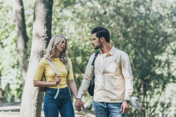 Retrato de pareja joven con mochilas cogidas de la mano en el parque - foto de stock