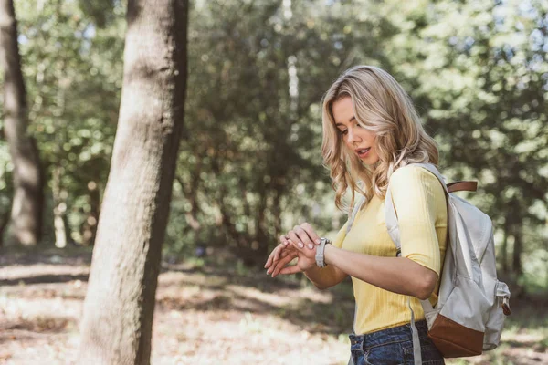 Vue latérale de la jeune femme avec sac à dos temps de contrôle dans le parc — Photo de stock