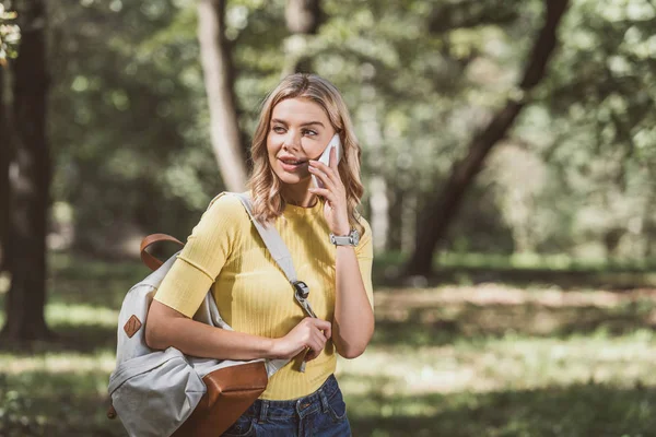 Porträt einer jungen Frau mit Rucksack, die im Park mit dem Smartphone spricht — Stockfoto