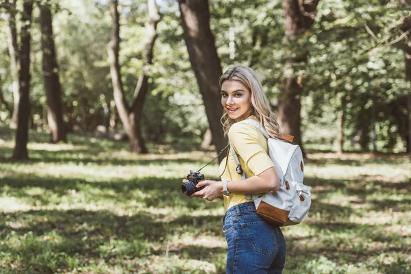 Jeune touriste souriant avec appareil photo et sac à dos dans le parc — Photo de stock