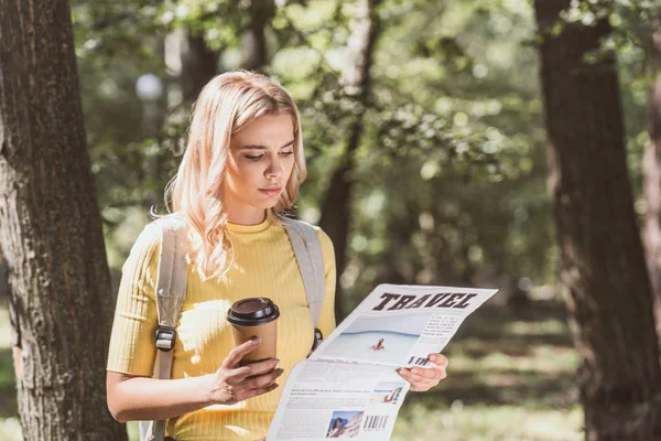 Ritratto di una giovane bionda con caffè per andare a girare il giornale nel parco — Foto stock