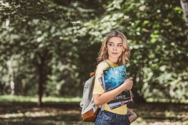 Ritratto di bella giovane donna con zaino e riviste in parco — Foto stock