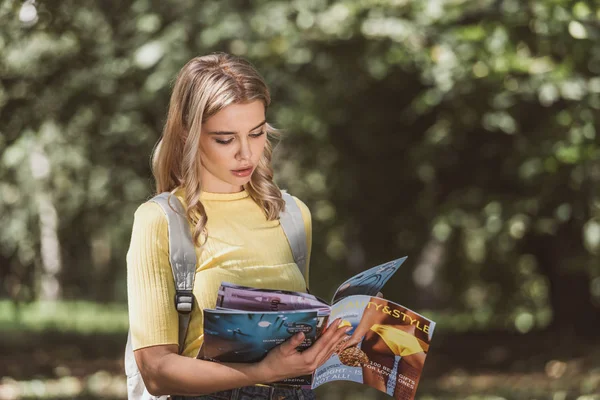 Retrato de una joven enfocada leyendo la revista en el parque - foto de stock